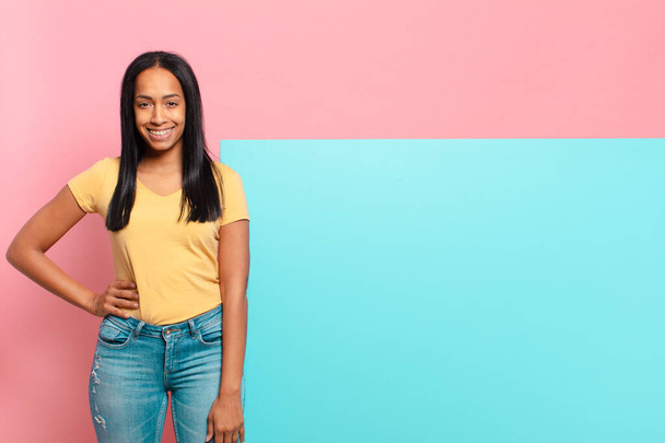 young black woman smiling happily with a hand on hip and confident, positive, proud and friendly attitude. copy space concept - Foto, Bild