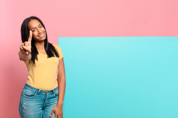 young black woman smiling and looking friendly, showing number one or first with hand forward, counting down. copy space concept - Photo, image