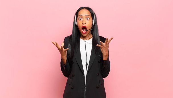 young black woman feeling extremely shocked and surprised, anxious and panicking, with a stressed and horrified look. telemarketing concept - Фото, зображення
