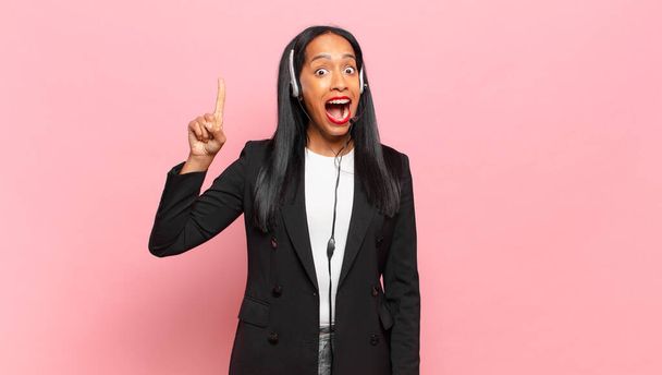 young black woman feeling like a happy and excited genius after realizing an idea, cheerfully raising finger, eureka!. telemarketing concept - Фото, изображение