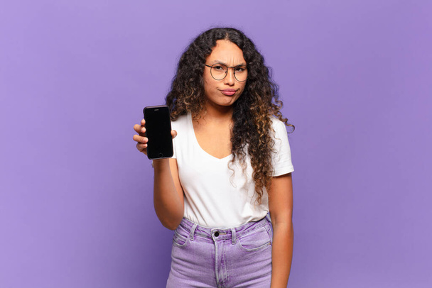 young hispanic woman feeling sad, upset or angry and looking to the side with a negative attitude, frowning in disagreement. smart phone concept - Photo, image