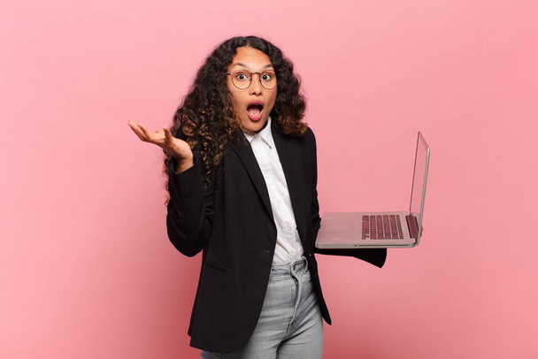 young hispanic woman open-mouthed and amazed, shocked and astonished with an unbelievable surprise. laptop concept - Foto, imagen