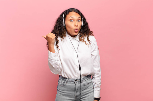 young hispanic woman looking astonished in disbelief, pointing at object on the side and saying wow, unbelievable. telemarketer concept - Foto, immagini