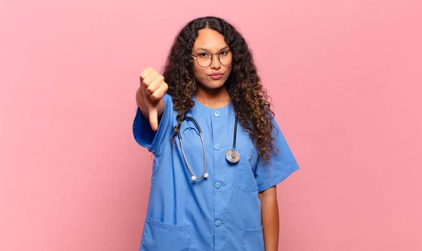 young hispanic woman feeling cross, angry, annoyed, disappointed or displeased, showing thumbs down with a serious look. nurse concept - Foto, imagen