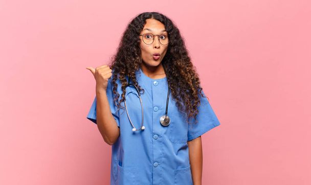 young hispanic woman looking astonished in disbelief, pointing at object on the side and saying wow, unbelievable. nurse concept - Fotografie, Obrázek