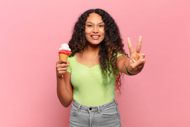 young hispanic woman smiling and looking friendly, showing number two or second with hand forward, counting down. ice cream concept - Φωτογραφία, εικόνα
