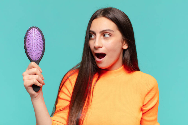 young pretty teenager girl. shocked or surprised expression. hair brush concept - Foto, Imagen