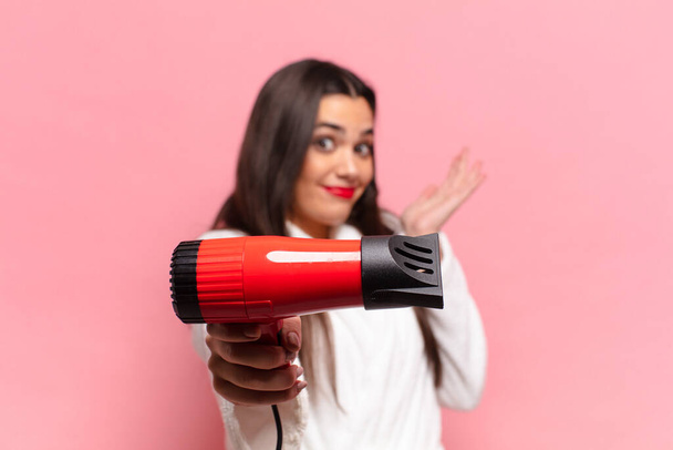 young pretty hispanic woman. happy and surprised expression. hair dryer concept - Foto, Bild