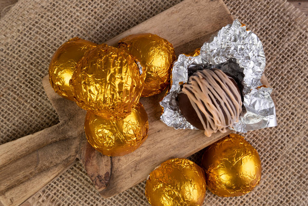chocolade truffels verpakt in gelamineerd papier op houten snijplank. - Foto, afbeelding