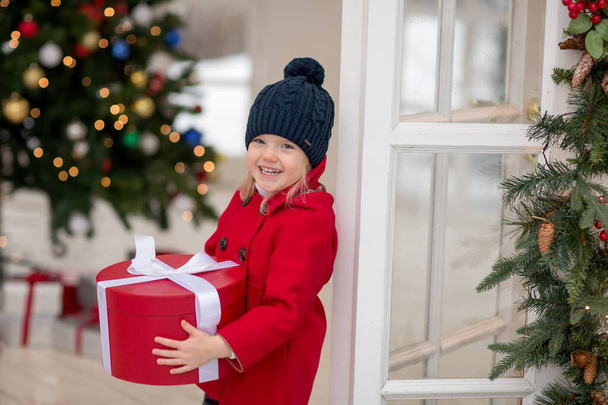 beautiful girl in A red coat standing on the street at the decorated Christmas tree holding a box with a gift - Valokuva, kuva
