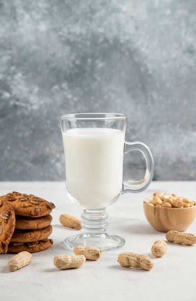Vaso de leche fresca y sabrosas galletas con cacahuetes sobre fondo de mármol. Foto de alta calidad - Foto, Imagen
