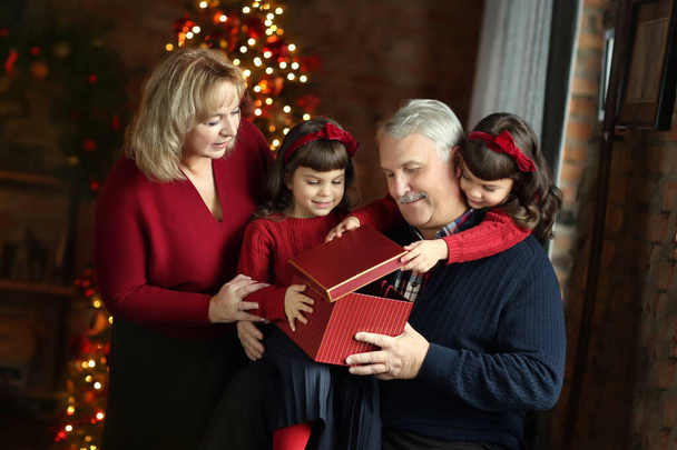 family, holidays, generation and people. Concept - smiling family with gift boxes sitting on sofa over living room with christmas tree background. Grandma gives a gift to granddaughters - Foto, Imagem