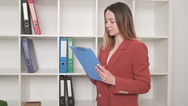 Χαριτωμένη γυναίκα συμπληρώνει έγγραφα στο γραφείο - Πλάνα, βίντεο