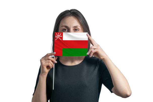 Glückliche junge weiße Frau mit Flagge Oman Flagge und bedeckt ihr Gesicht damit isoliert auf weißem Hintergrund. - Foto, Bild