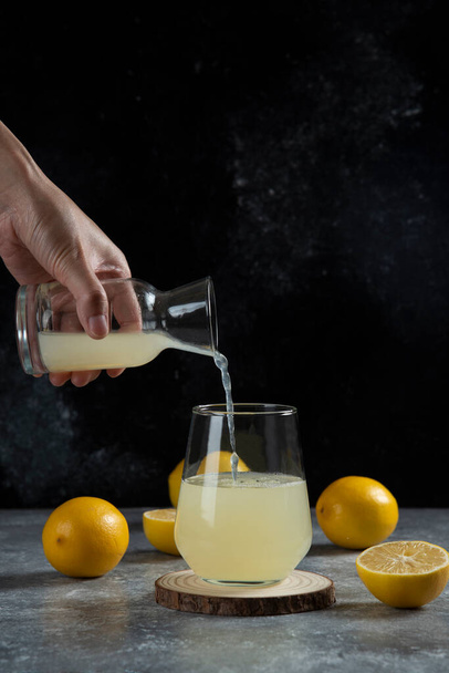 Una mano vertiendo jugo de limón en una taza de vidrio. Foto de alta calidad - Foto, Imagen