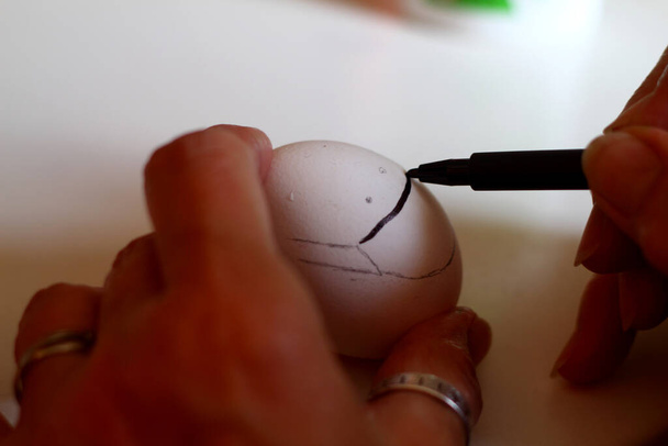 女性の手でイースターエッグを描きます。多色の背景にイースターの装飾を準備します。卵にN95マスクを描いてる. - 写真・画像