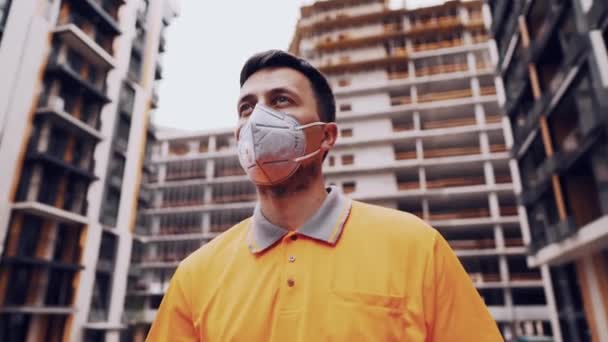 Koronavirüs, covid-19, hava kirliliği, toz, inşaat ve imalatta alerji. Çalışanların sağlık koruması. İnşaatçı inşaat alanında kask takar ve 95 numaralı koruyucu maskeyi takar. - Video, Çekim