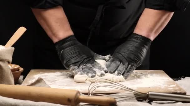 chef en guantes de látex negro amasando masa de harina de trigo blanco en una tabla de madera, preparando masa de pizza - Imágenes, Vídeo