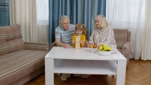 Mayores abuelos pareja con niño nieta jugando juego con bloques de madera en casa - Metraje, vídeo