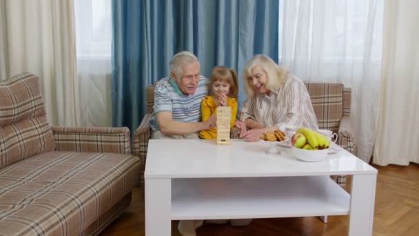 Senior pareja abuelos y nieta disfrutando de juego de mesa torre de construcción de bloques en casa - Metraje, vídeo