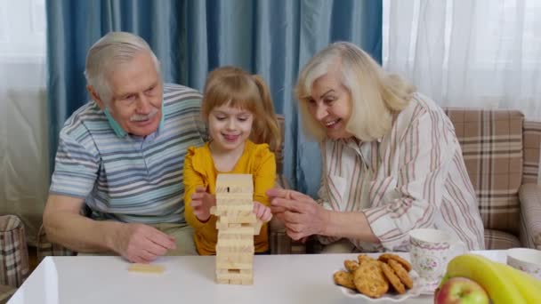 Emocionado niño niña involucrada en bloques de construcción juego de mesa con la abuela y el abuelo senior - Imágenes, Vídeo