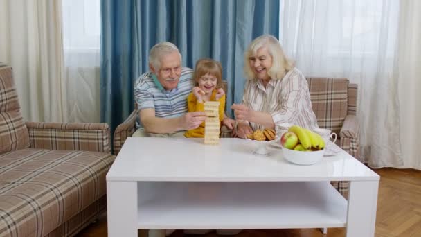 Senior ζευγάρι παππούδες και γιαγιάδες με παιδί εγγονή παίζουν παιχνίδι με ξύλινα μπλοκ στο σπίτι - Πλάνα, βίντεο