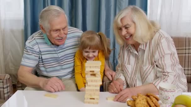Ηλικιωμένοι παππούδες ζευγάρι και εγγονή απολαμβάνοντας επιτραπέζιο παιχνίδι κτίριο πύργο από μπλοκ στο σπίτι - Πλάνα, βίντεο