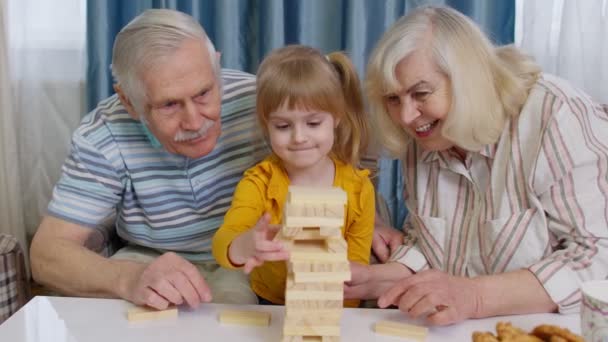 Podekscytowany dziecko dziewczynka zaangażowana w budowanie bloków gra planszowa z babcią i dziadkiem - Materiał filmowy, wideo