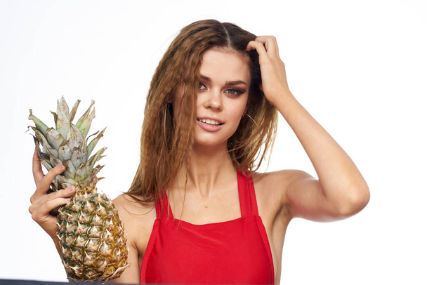Woman with pineapple in hands wavy hair red t-shirt fruits summer vacation light background - Foto, imagen