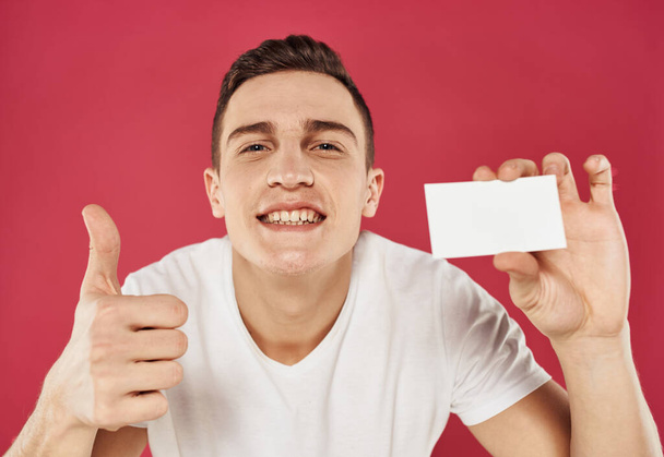 A guy with a business card in his hand gestures and emotions red background - Foto, Imagem