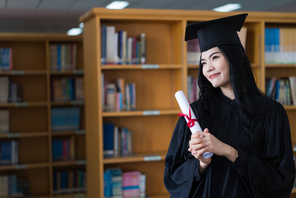 Una joven asiática feliz graduada universitaria en vestido de graduación y gorra lleva una máscara facial tiene un certificado de grado para celebrar su logro educativo en el día del comienzo. Foto de stock - Foto, imagen