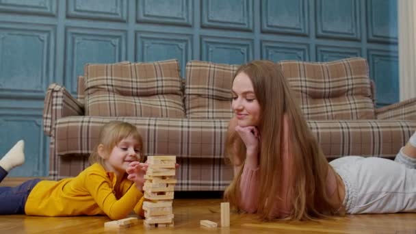 Feliz joven madre mujer enseñando niño pequeño hija jugando bloques de madera juego de mesa en casa - Metraje, vídeo