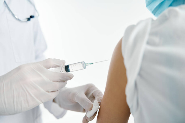 лікар в захисних рукавичках вводить вакцину в плече пацієнта жінки в лікарняній ковдрі
  - Фото, зображення