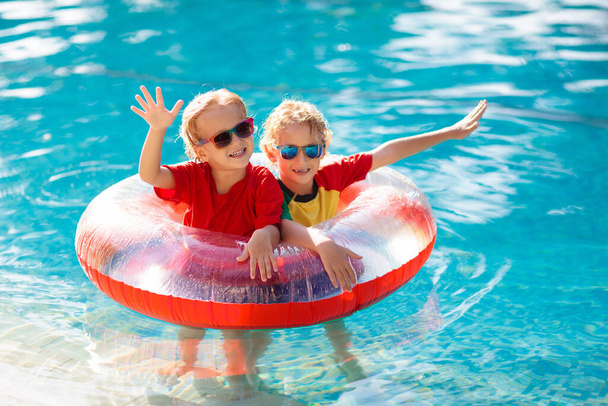 Gyerekek játszanak szabadtéri medence trópusi üdülőhely. Úszó segédeszköz kisgyereknek. A baba búvárkodni tanul. Egy csapat gyerek játszik a vízben. Színes mentőmellény. Strand és nyári szórakozás. - Fotó, kép