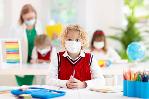 Kids in face mask in school class. Child back to school after coronavirus lockdown. Primary child in covid-19 pandemic. Safety and virus spread prevention. Student in surgical mask. Social distancing. - Photo, Image