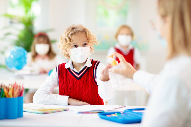 Kids in face mask in school class. Teacher with hand sanitizer. Sanitizing in school. Student child in coronavirus lockdown. Primary child in covid-19 pandemic. Safety and virus spread prevention.  - Photo, Image