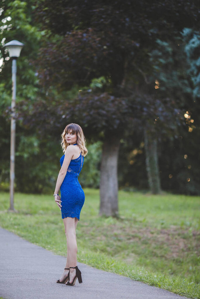 A vertical shot of a Caucasian sexy woman with blonde hair and blue dress on the nature background. - Fotó, kép