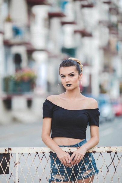 A vertical shot of a Caucasian sexy woman with black lipstick leaning on a fence - Фото, зображення