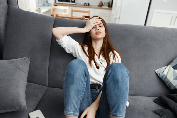 woman sitting on the couch feeling unwell hand on face stress - Fotó, kép