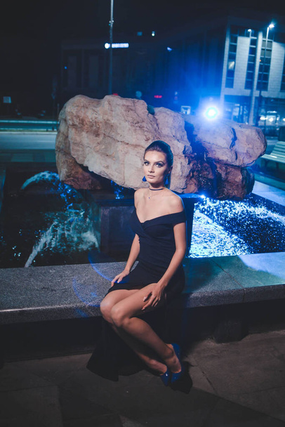 A portrait of a Caucasian sexy woman with a black dress sitting on the fountain wall - Fotoğraf, Görsel