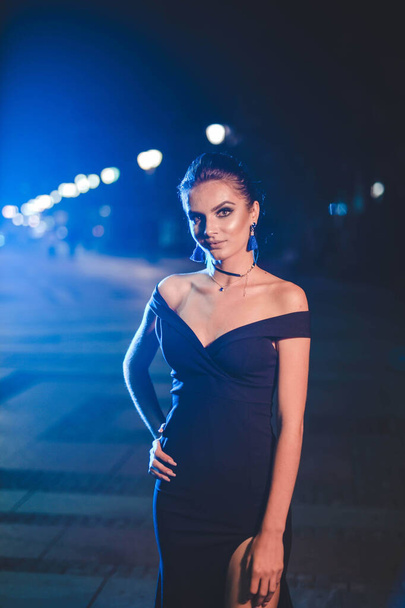 A vertical shot of a Caucasian sexy, attractive woman on the blue street lights background - Fotó, kép