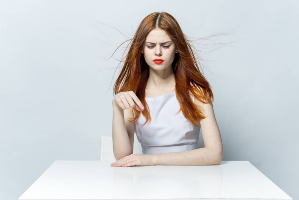 όμορφη κοκκινομάλλα γυναίκα κάθεται στο τραπέζι χειρονομία χέρια συναισθήματα και κόκκινα χείλη μοντέλο - Φωτογραφία, εικόνα