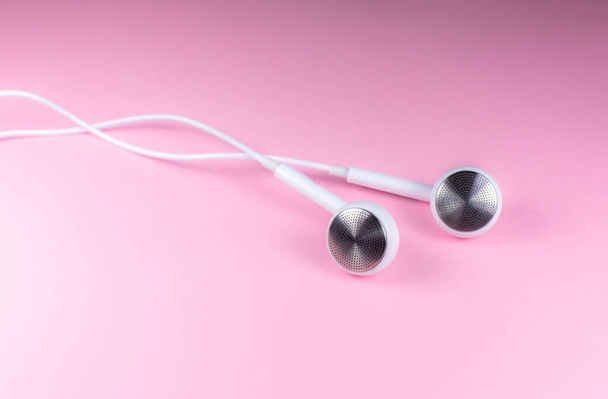 White Earphones lying on the pink background. Modern music concept. Audio technology. Close up photo. - Photo, Image