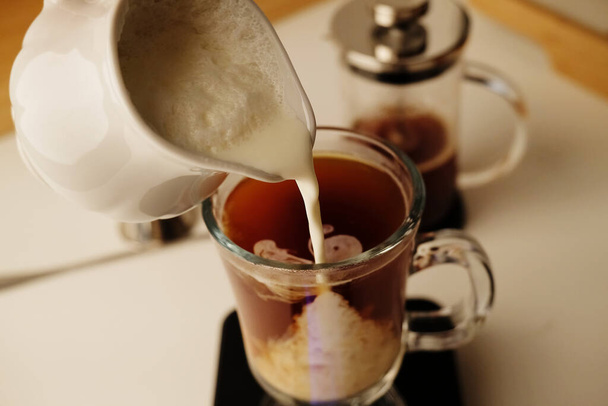 Melk koffie bereidingsproces. Lichte slagroom wordt in de koffie gegoten. Latte in een Iers glas - Foto, afbeelding