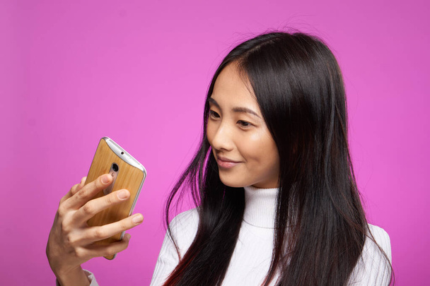 fröhliche hübsche Brünette mit einem Telefon in ihren Händen Kommunikation Internet-Technologie rosa Hintergrund - Foto, Bild