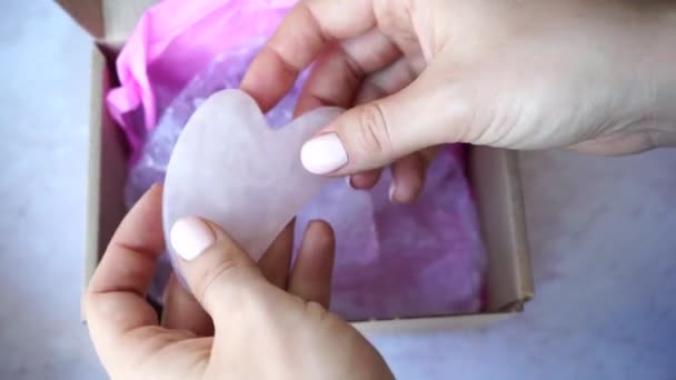 Gua Sha massager νεφρίτη ρολό σε γυναικεία χέρια. Ροζ πέτρα νεφρίτη για περιποίηση προσώπου και σώματος - Πλάνα, βίντεο
