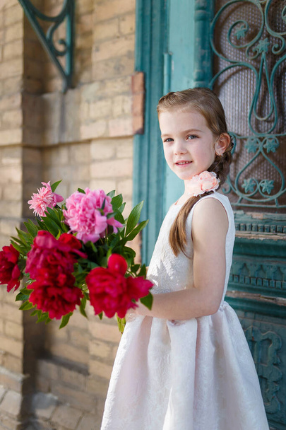 Bella bambina in abito bianco con grande bouquet di peonie. Fioritura primaverile e concetto di infanzia spensierata. - Foto, immagini