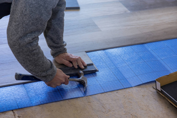 Renovatie werken ambachtsman verbetering man met een met behulp van hamer de installatie laminaat vloeren in nieuw appartement - Foto, afbeelding