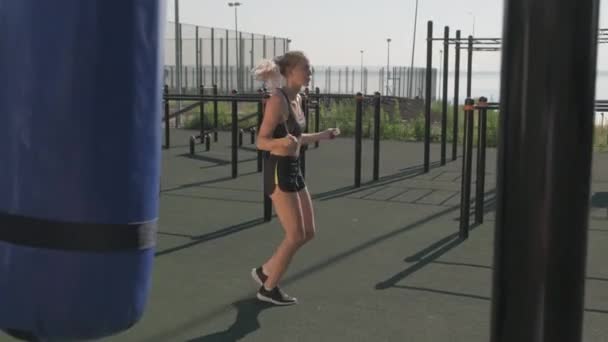 Volledige handheld shot van vastberaden jonge sportvrouw springtouw buiten op sportveld in de zomer, het dragen van strakke gewas top en korte broek - Video