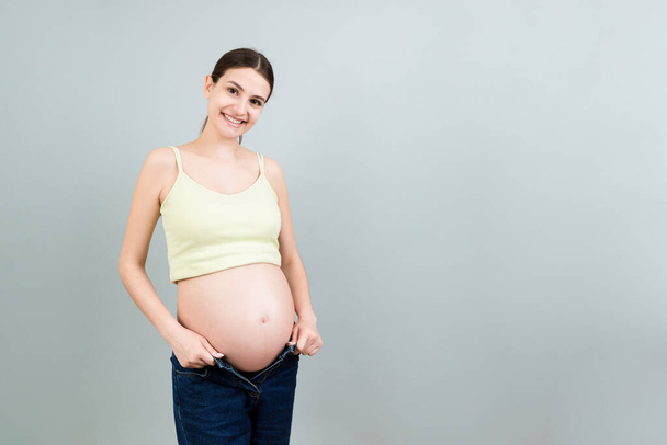 Mulher grávida feliz em jeans descompactados mostrando sua barriga nua em fundo colorido com espaço de cópia. Bebê esperando conceito. - Foto, Imagem